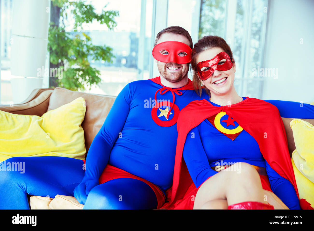 Pareja de superhéroes sonriendo en el sofá de la sala Foto de stock