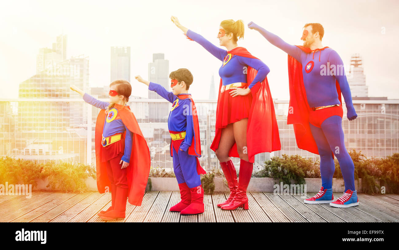 La familia de superhéroes de pie con los brazos extendidos sobre la azotea de la ciudad Foto de stock