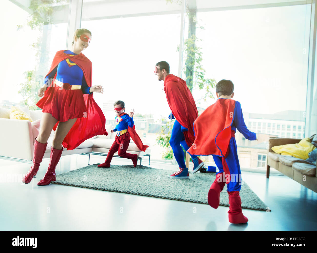 La familia de superhéroes persiguiendo unos a otros en la sala de estar Foto de stock