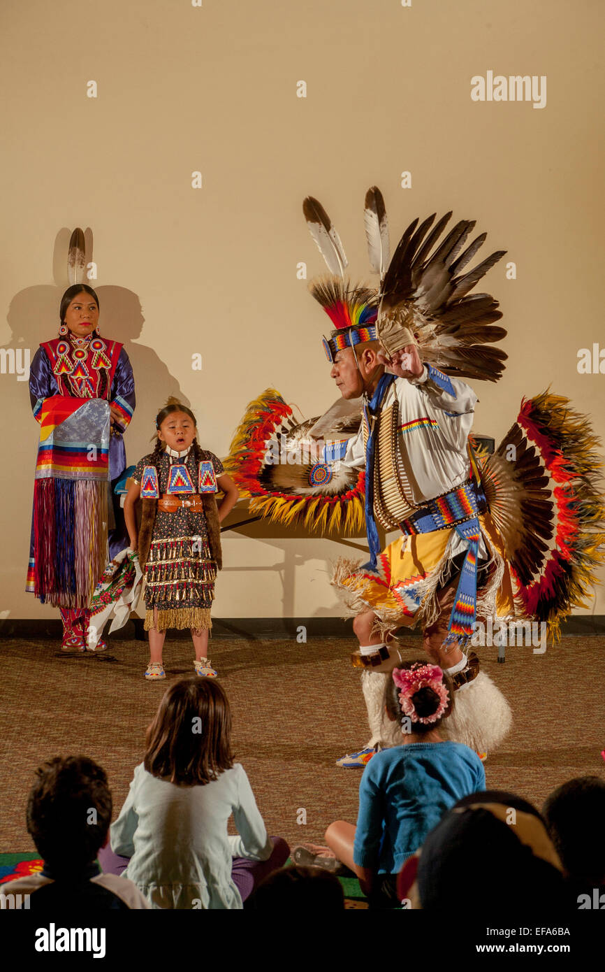 Como los niños en la audiencia watch, un Indio Navajo bailarín vistiendo trajes tribales completo realiza el Fancy Thunder Dance durante una velada de la cultura Nativa Americana en la Laguna Niguel, CA, biblioteca pública. Nota murgas hijas. Foto de stock