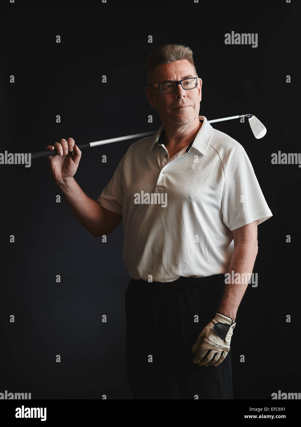 Hombre maduro golfista llevaba una camisa blanca y mantenga un club de golf de hierro sobre su hombro - studio shot, fondo negro Foto de stock