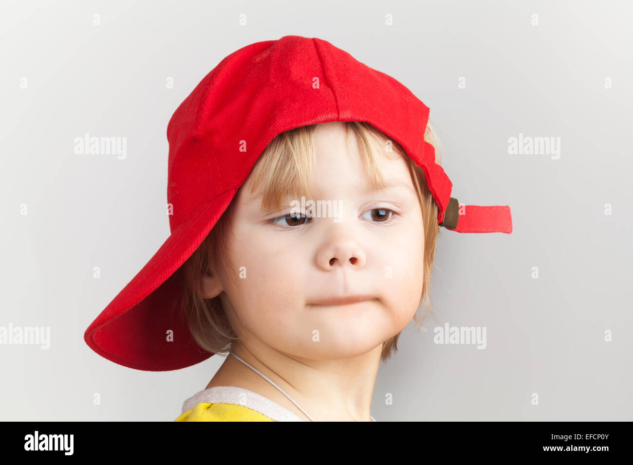 Retrato de estudio de Funny Baby Girl en una gorra de béisbol roja sobre fondo de pared gris Foto de stock