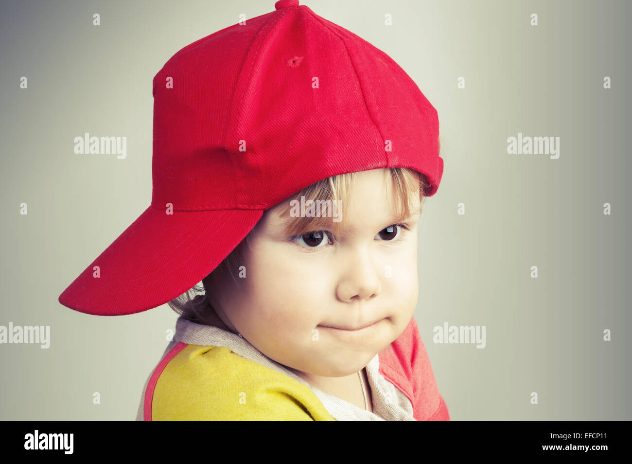 Retrato de estudio de Funny Baby Girl en rojo gorra de béisbol a lo largo de pared gris de fondo. Estilo Vintage, tonifica Efecto Filtro de fotos Foto de stock