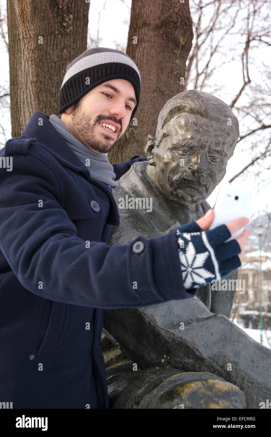 Joven barbudo teniendo un gracioso selfie con un monumento en el parque Foto de stock