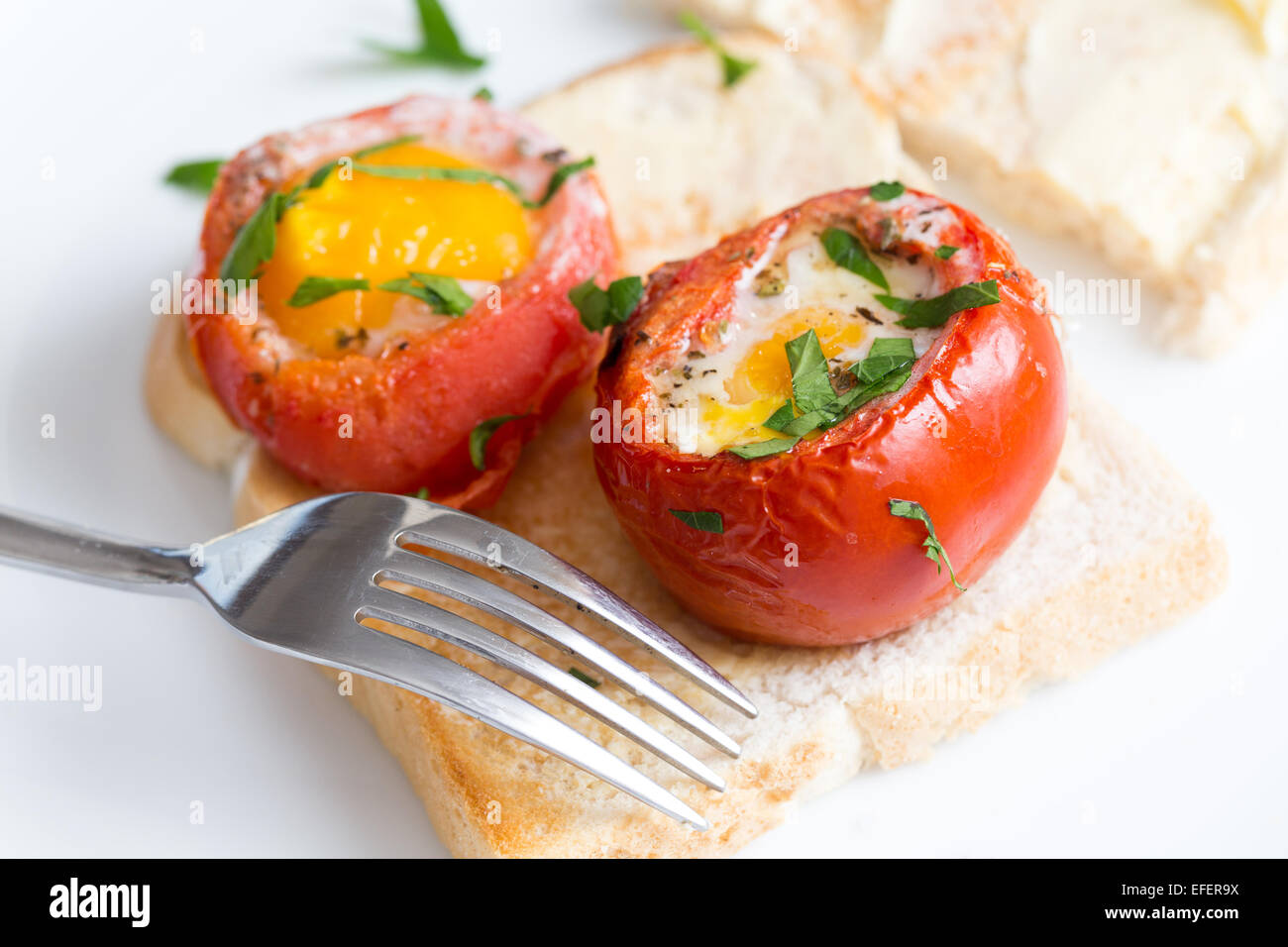 Cocido, de-sembró tomates rellenos con un huevo y terminado en el horno,  servido sobre una tostada con una guarnición de perejil. Este plato  italiano Fotografía de stock - Alamy