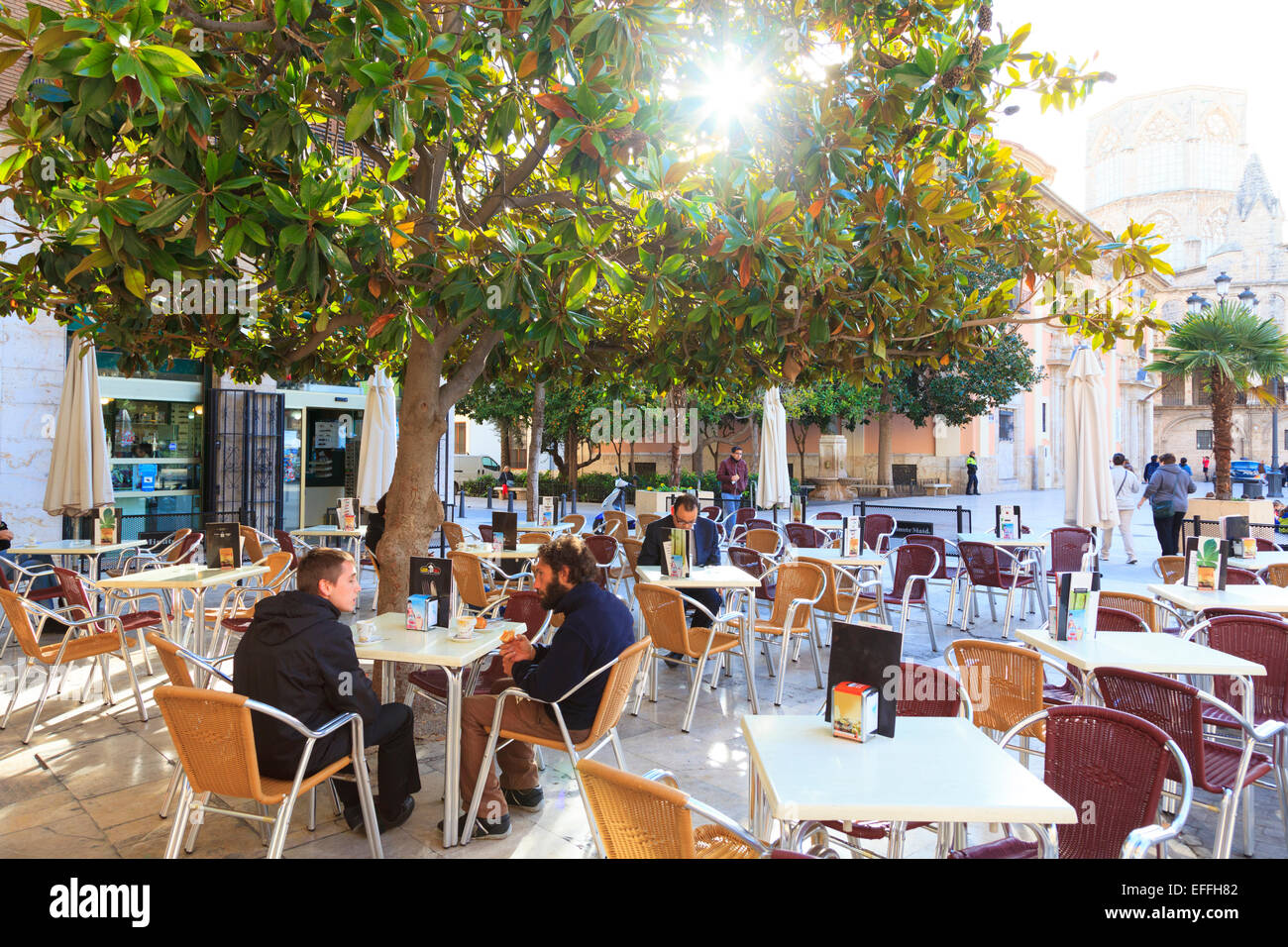 Los clientes en una cafetería de la calle en la Plaza de la Seu con sun vislumbrando a través de árboles Foto de stock