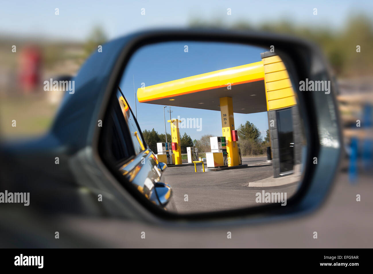Reflejo de la gasolinera del lado del vehículo en el espejo. El enfoque selectivo. Gasolinera con dispensador y bombas. Foto de stock