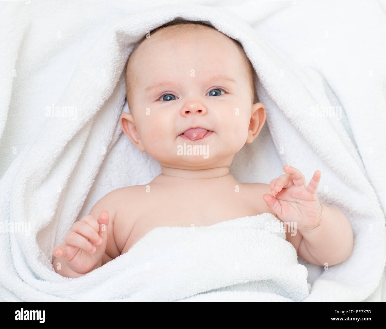 Lindo gracioso bebé en una toalla de baño mostrando lengua Foto de stock