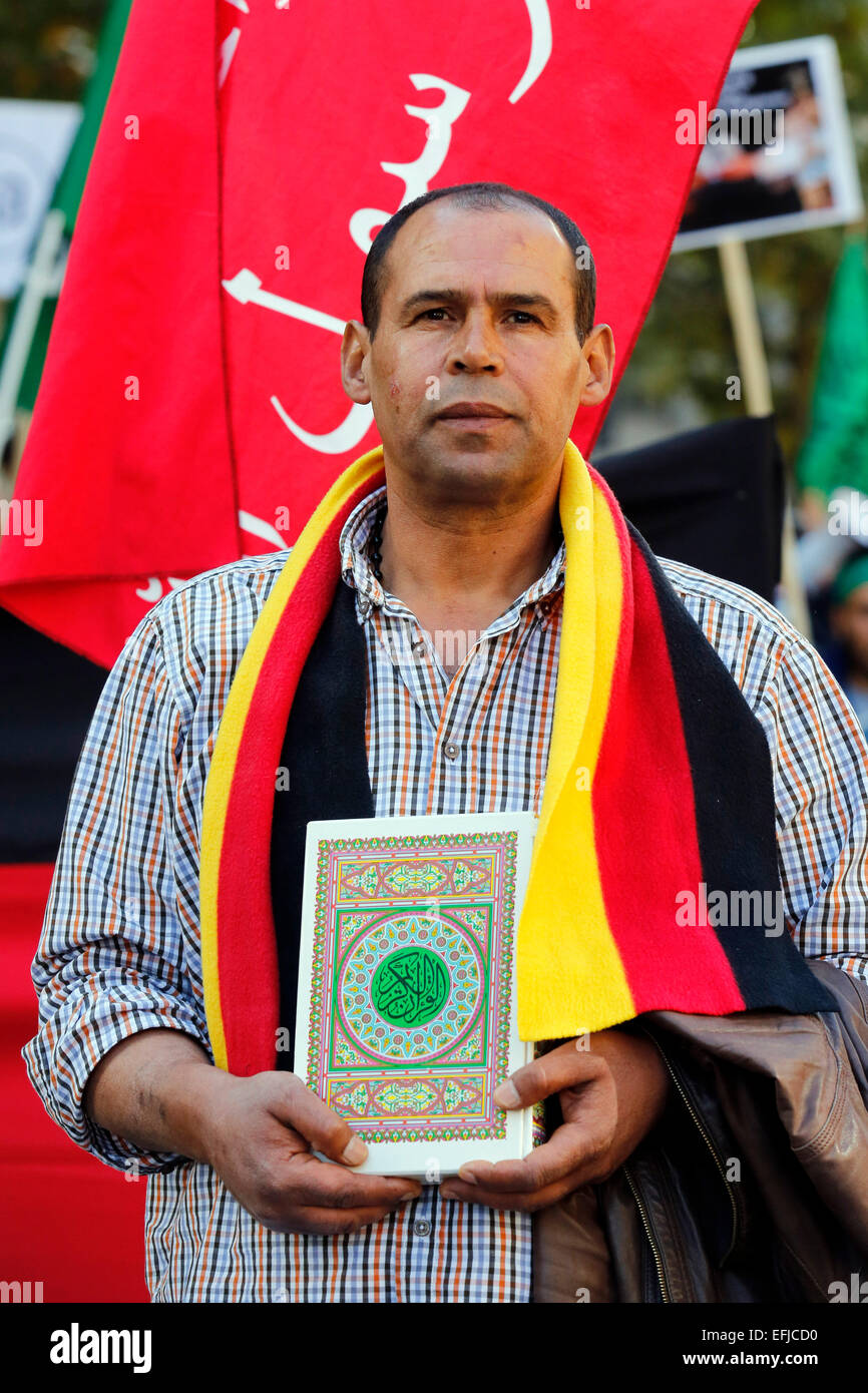 Turco hombre vestido con bufanda en alemán banderas de colores (negro oro rojo) mantiene el Corán, el libro sagrado de los musulmanes en sus manos. Dortmund/Alemania. Foto de stock