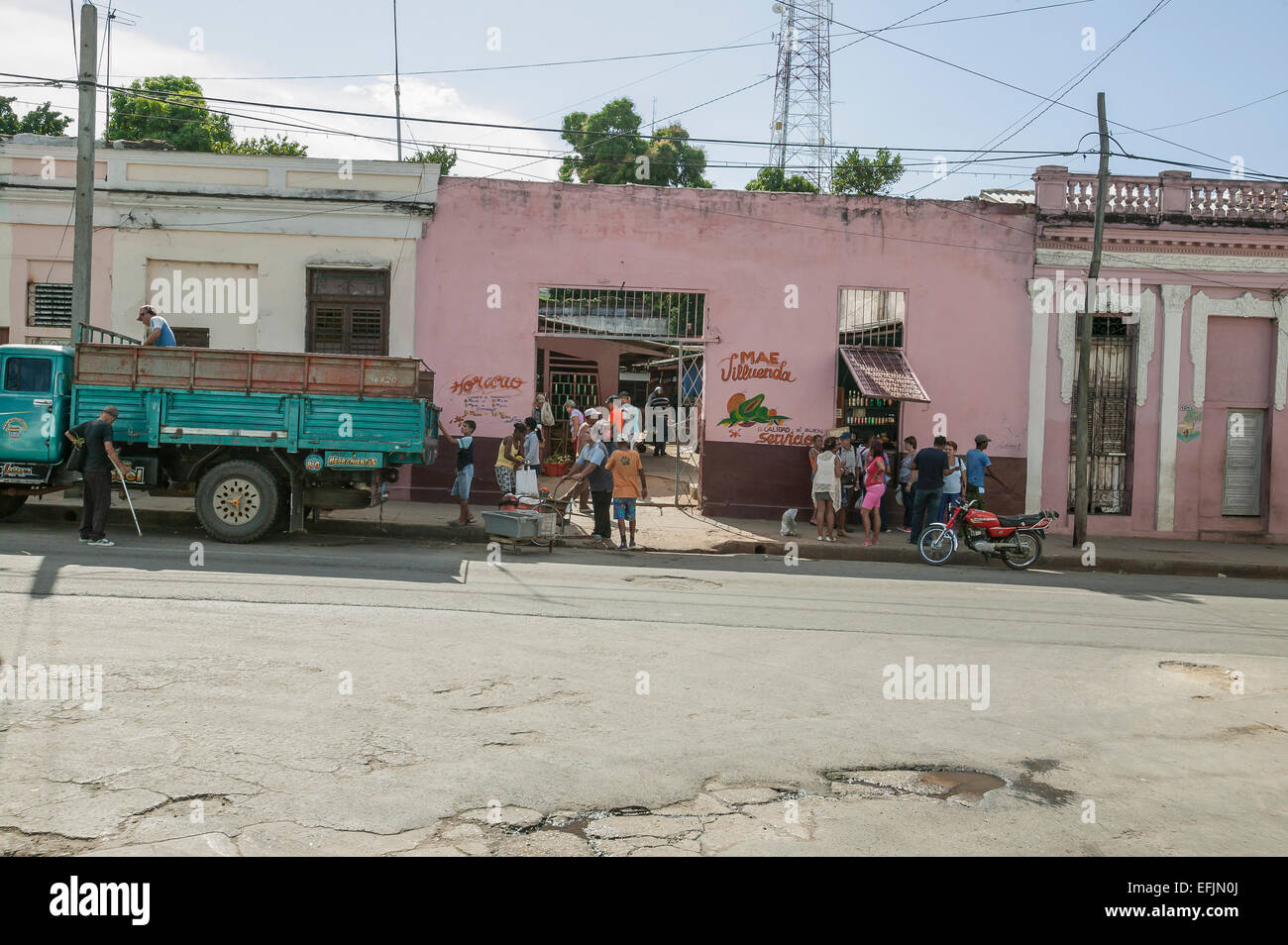 Los hombres cubanos descarga de productos frescos de un camión de entrega en frente de un mercado con muchos Cubanos compras en Cienfuegos, Cuba Foto de stock