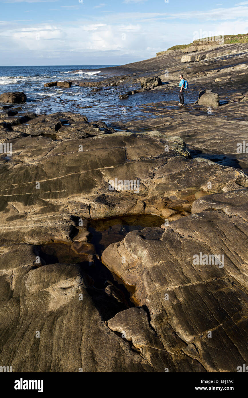 Persona de pie sobre las rocas expuestas al mal, la bahía de la costa de Clare, Irlanda Foto de stock