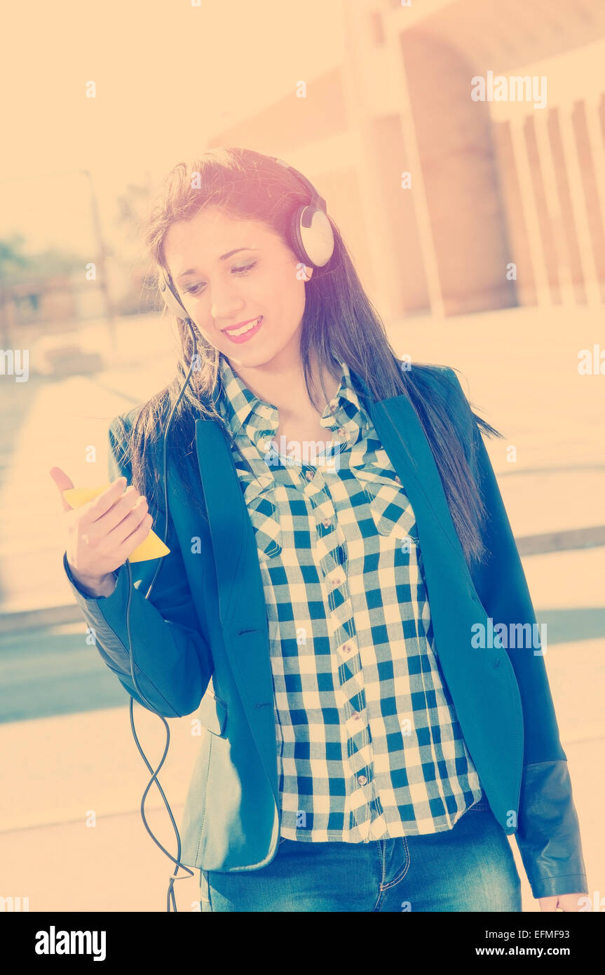 Urban hermosa morenita chica escuchando música a través de auriculares y estilo instagram filtro aplicado un efecto flare Foto de stock