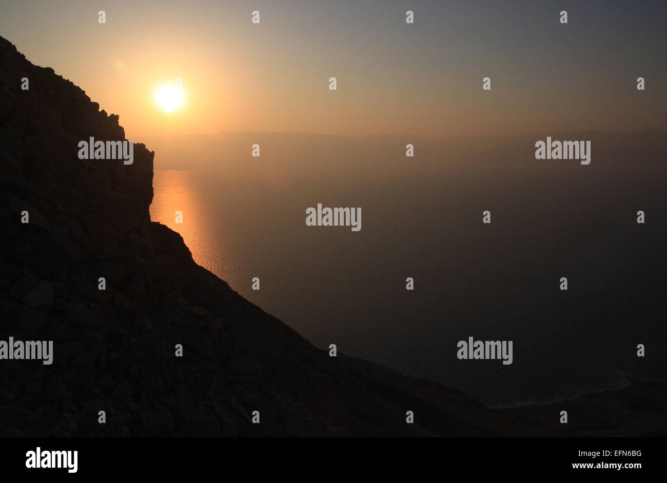 El Sol se eleva sobre el Mar Muerto. Una silueta de montaña se encuentra en la parte delantera. Foto de stock