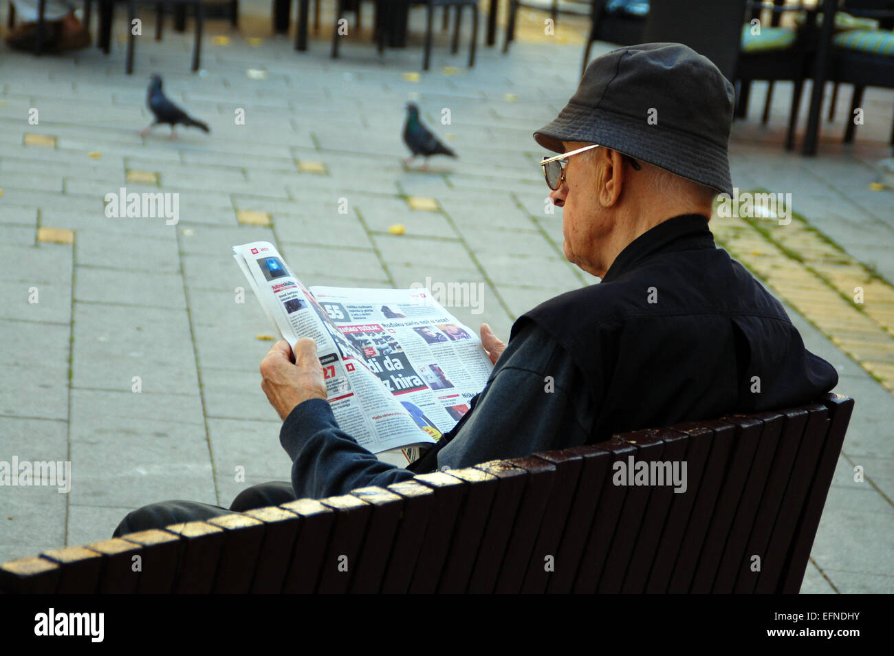 En una relajada tarde de verano y el hombre de negro que lee el periódico en un banco en el centro de la ciudad. Foto de stock