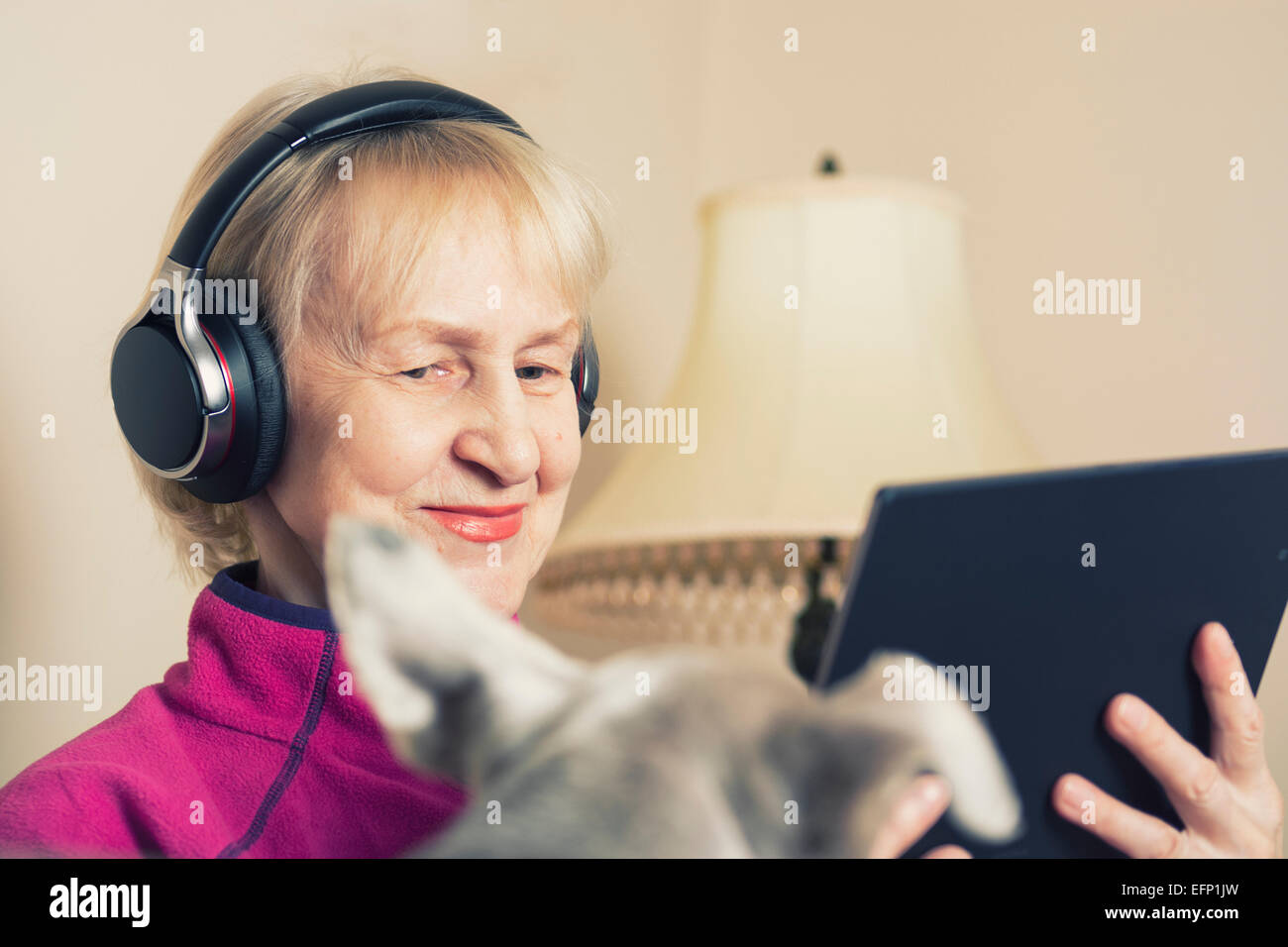 Mujer mayor Caucásica Feliz Smiling usando auriculares de sujeción tableta Foto de stock