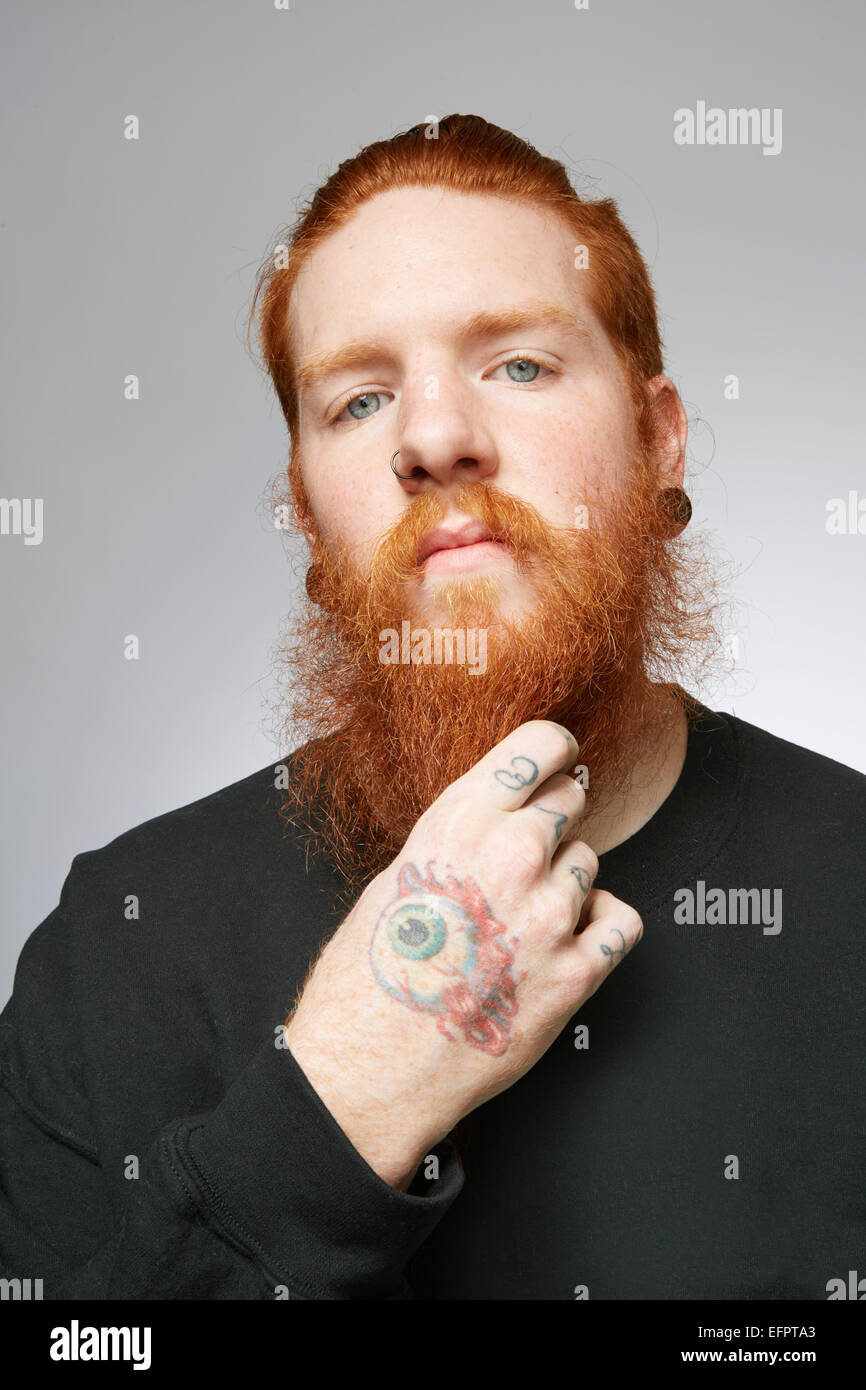 Retrato de estudio de joven con pelo rojo acariciando la barba Foto de stock