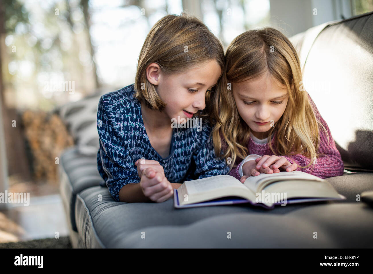 Dos chicas rubias, acostado en un sofá, mirando un libro. Foto de stock
