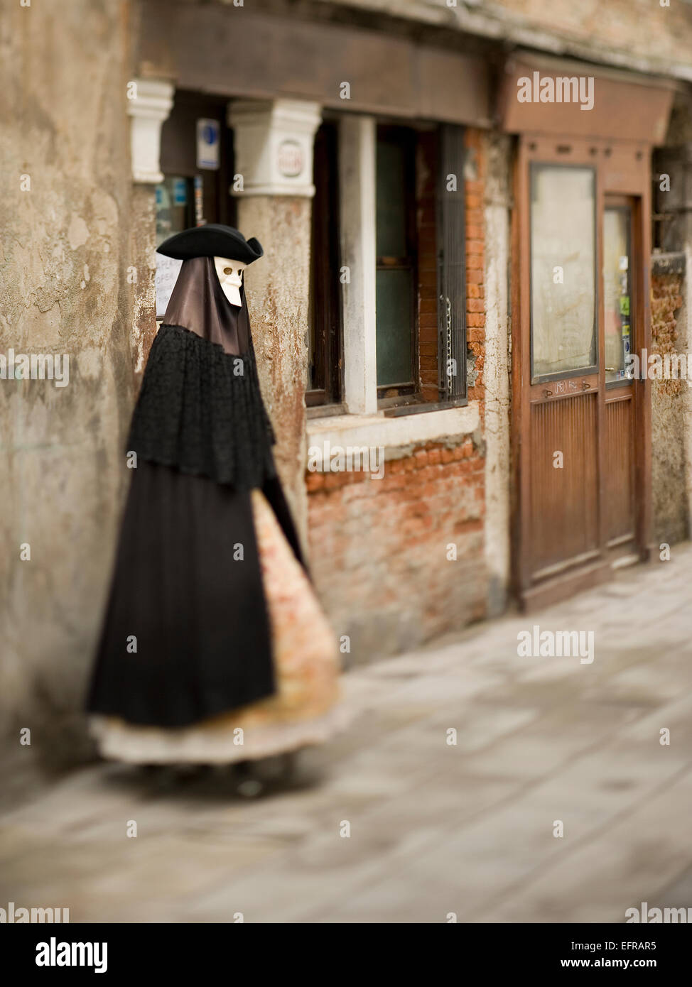 Una persona en disfraz de carnaval, máscara, sombrero y manto en Venecia de pie en la calle Foto de stock