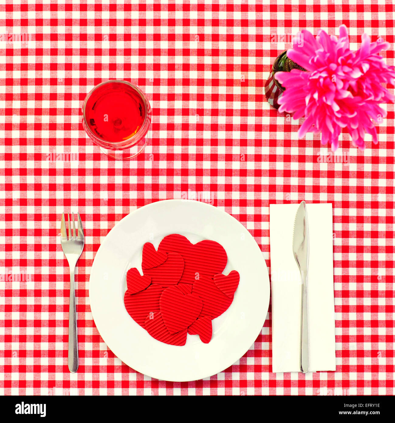 Disparo de alto ángulo de un plato lleno de Corazones rojos con tamaño diferente en una mesa con un mantel a cuadros rojo y blanco Foto de stock
