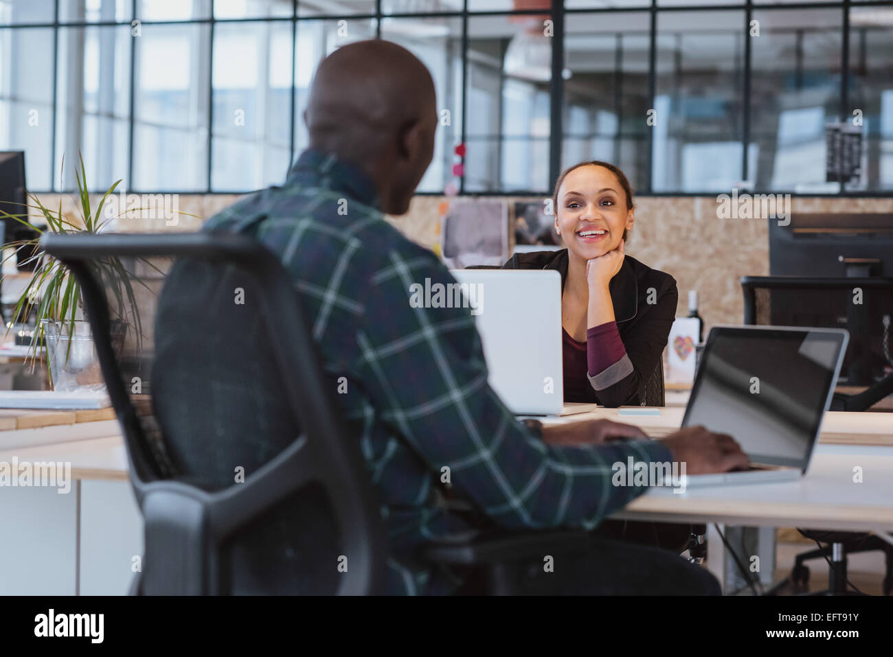 Joven africana sentados en la mesa hablando de trabajar con colega varón sonriendo. Las personas creativas que trabajan en la oficina. Foto de stock