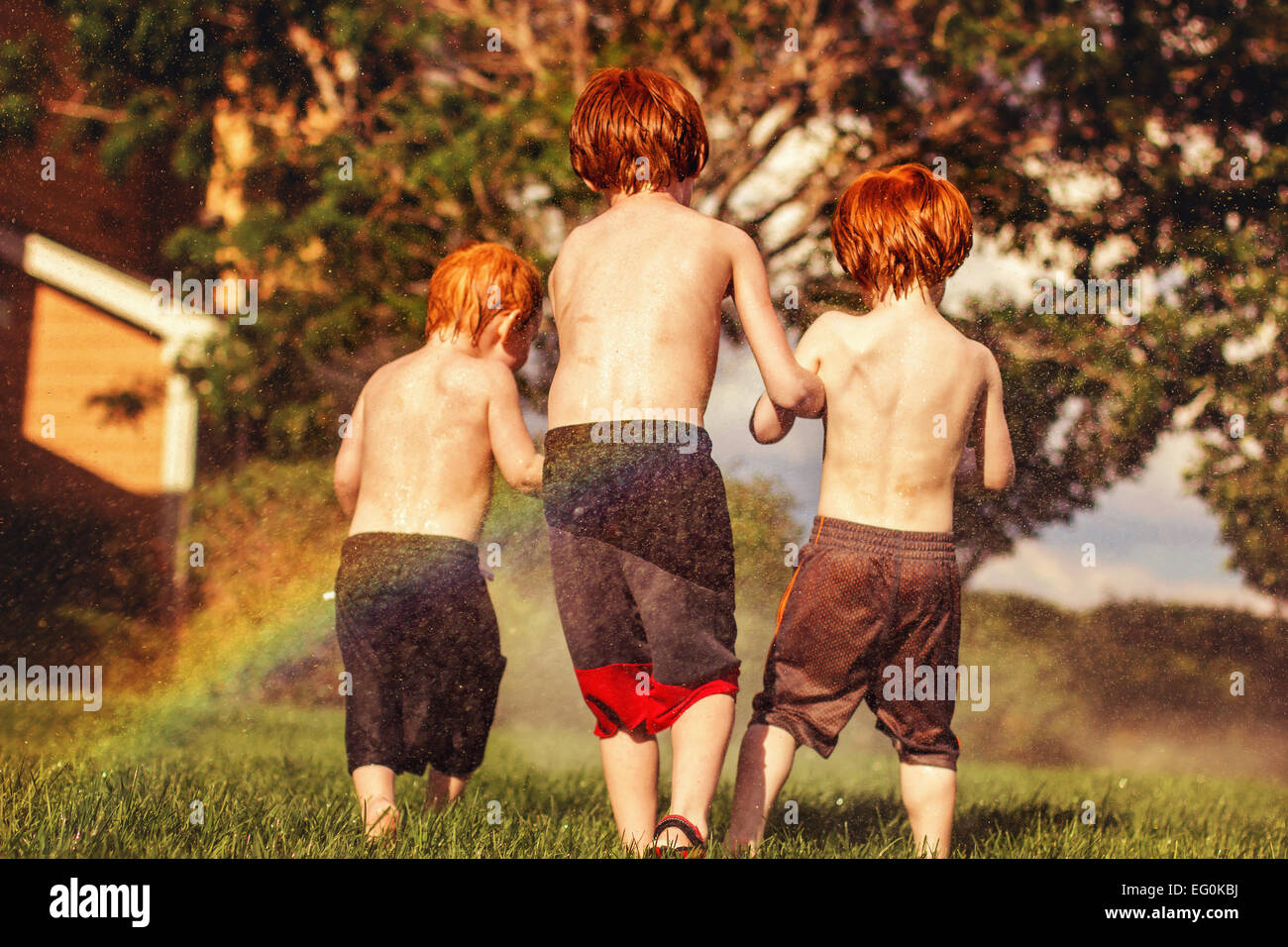Tres jóvenes hermanos jugando en rociadores de agua Foto de stock