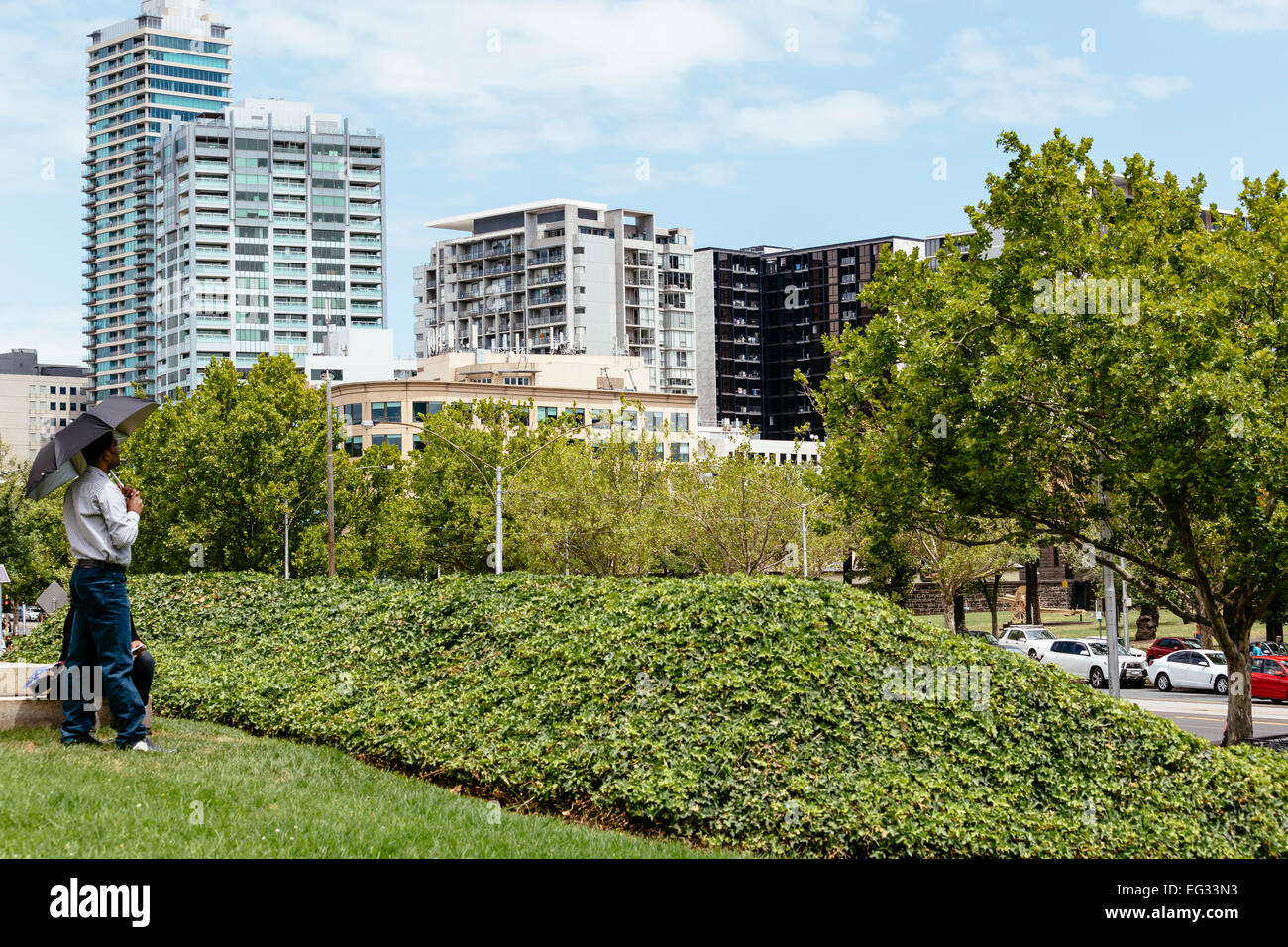 Hombre con sombrilla mirando por encima de St Kilda Rd desde Kings Domain en Melbourne. Foto de stock