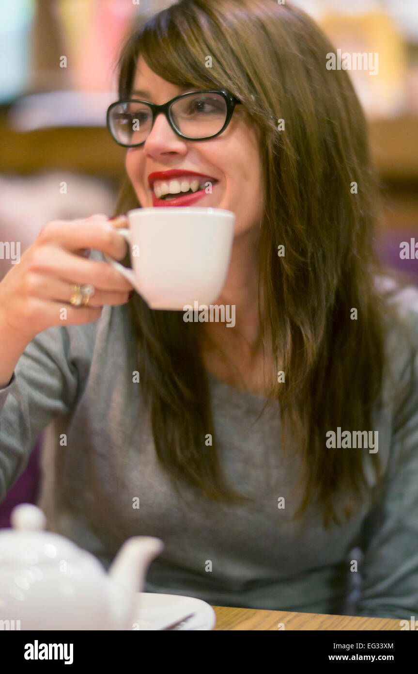 Hermosa joven disfrutando de una bebida caliente con amigos en un acogedor café. Foto de stock