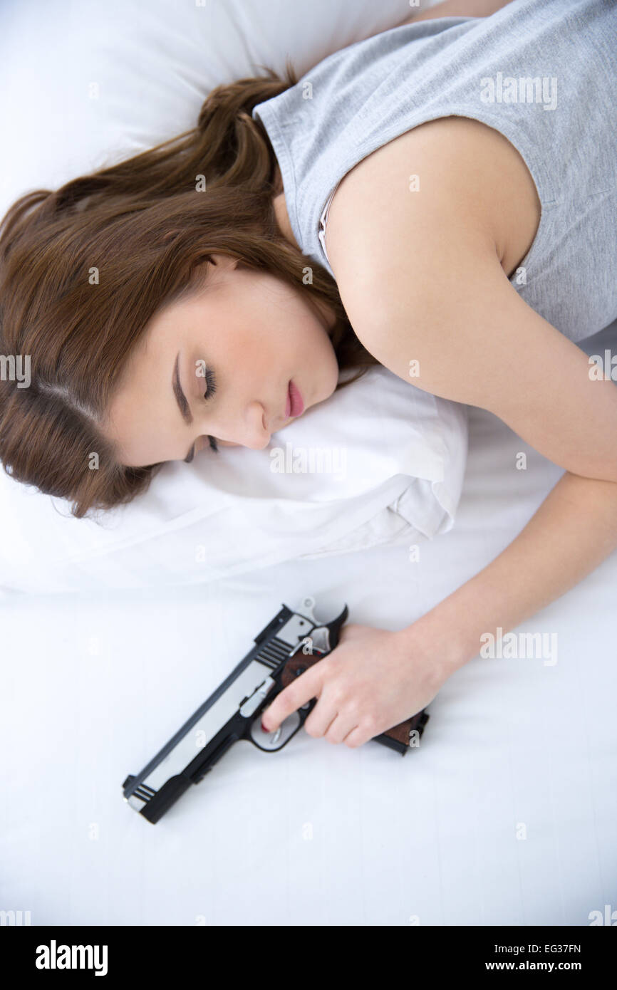 Mujer duerme en la cama con la mano en pistolas de seguridad en el hogar Foto de stock