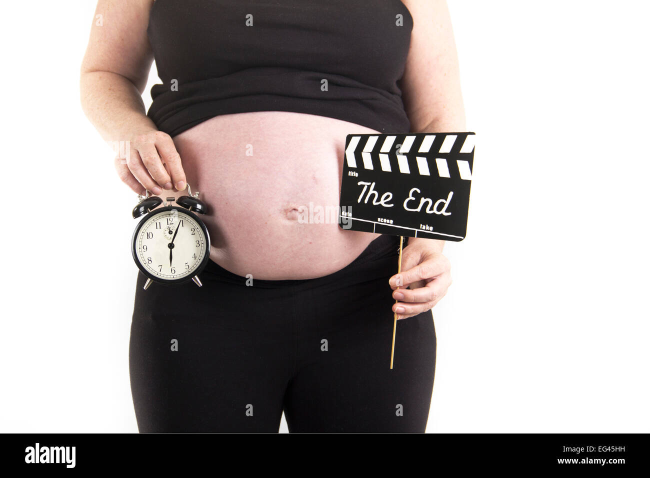 Mujer embarazada sujetando el reloj y el final signo delante del vientre Foto de stock