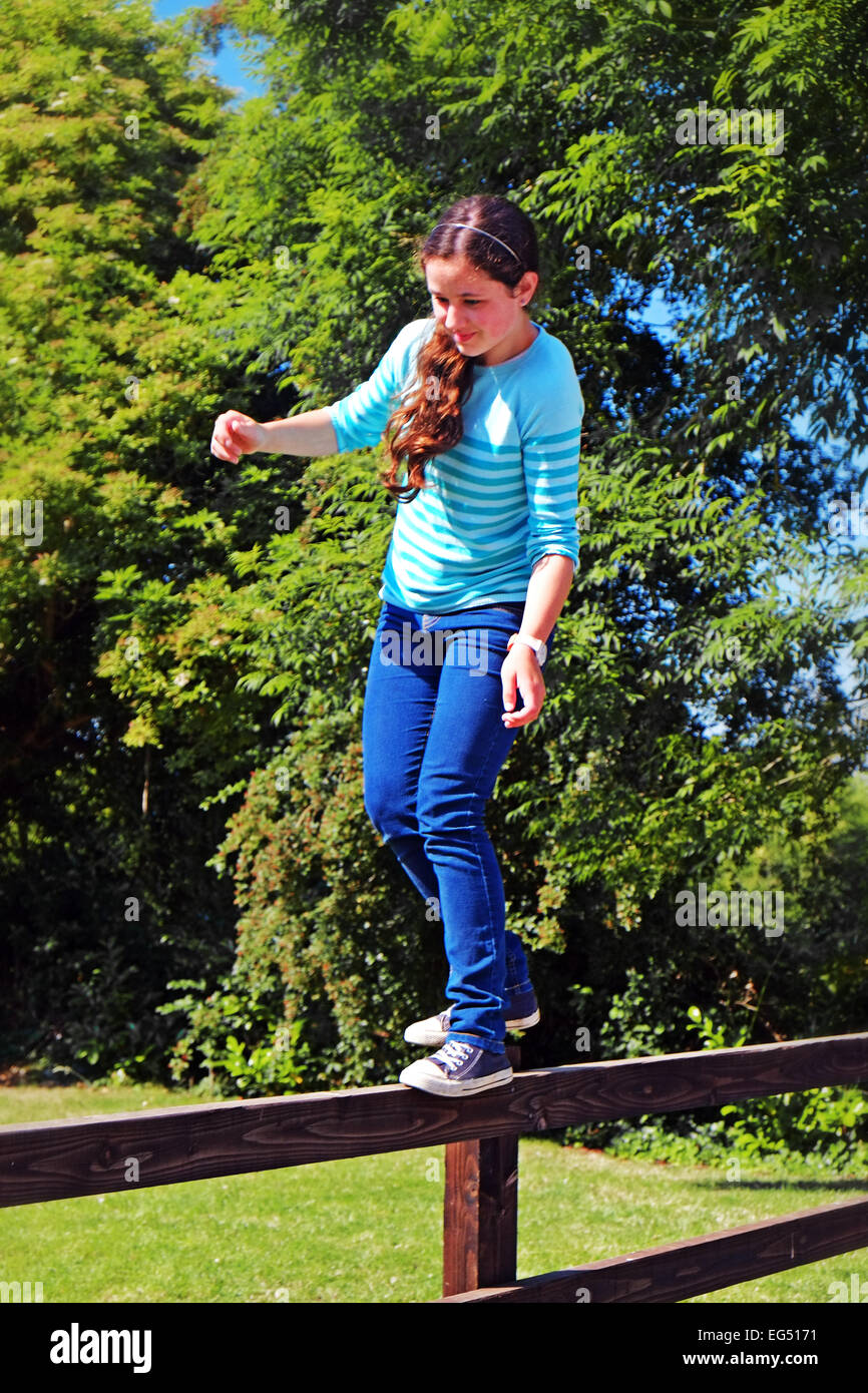 Joven chica irlandesa cuerda floja en una valla de madera en su jardín en la Irlanda rural Foto de stock