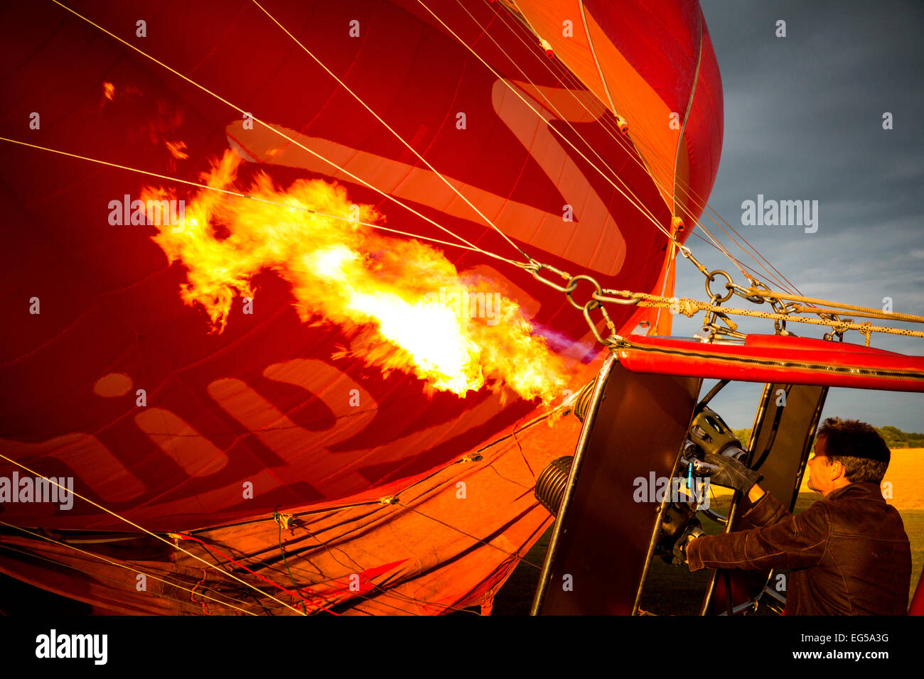 El hombre controla el quemador de gas las llamas rojas de inflar un globo de aire caliente, south oxfordshire, Inglaterra Foto de stock