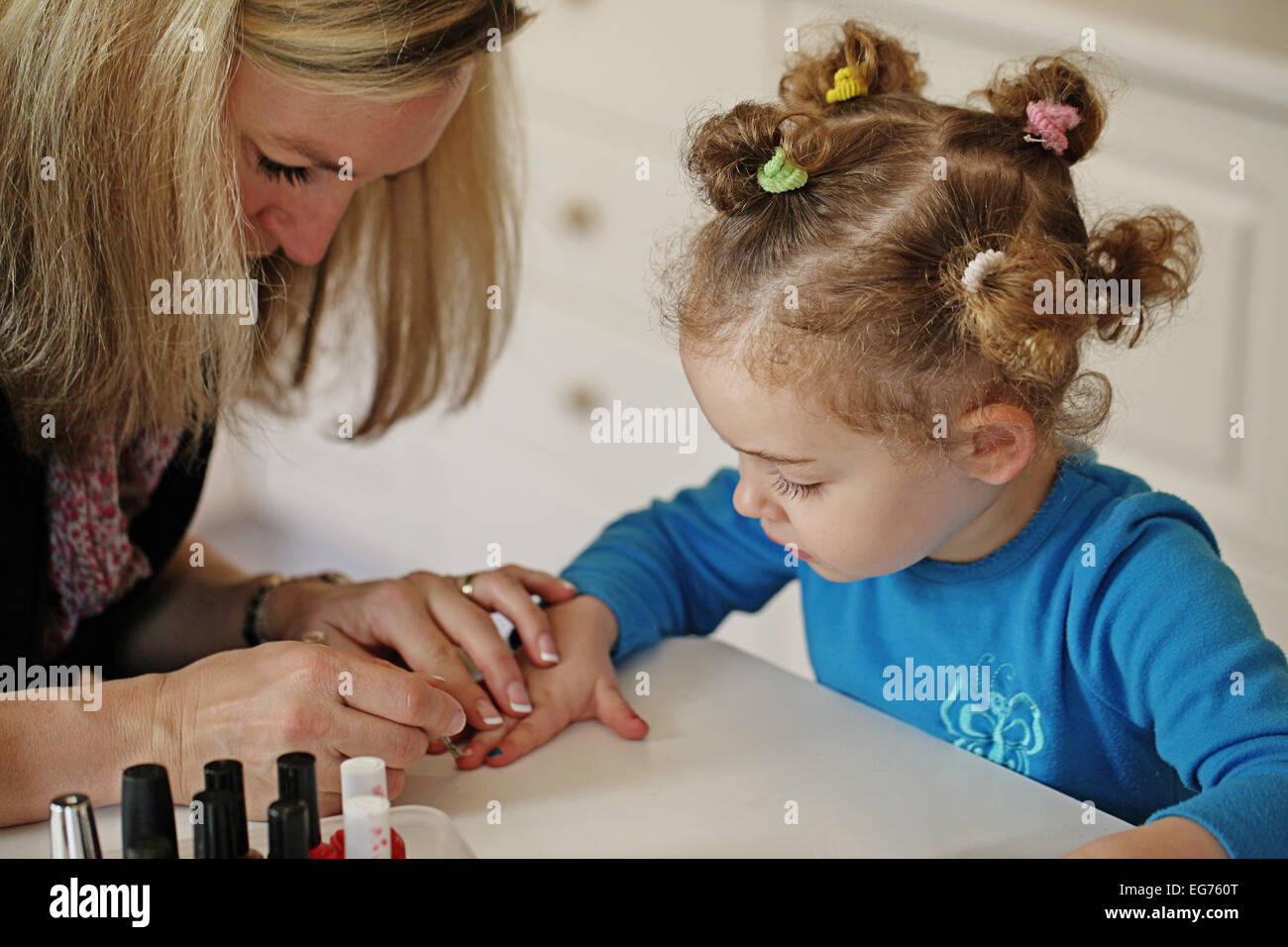 Mamá rubia pintura las uñas de su hija. Foto de stock