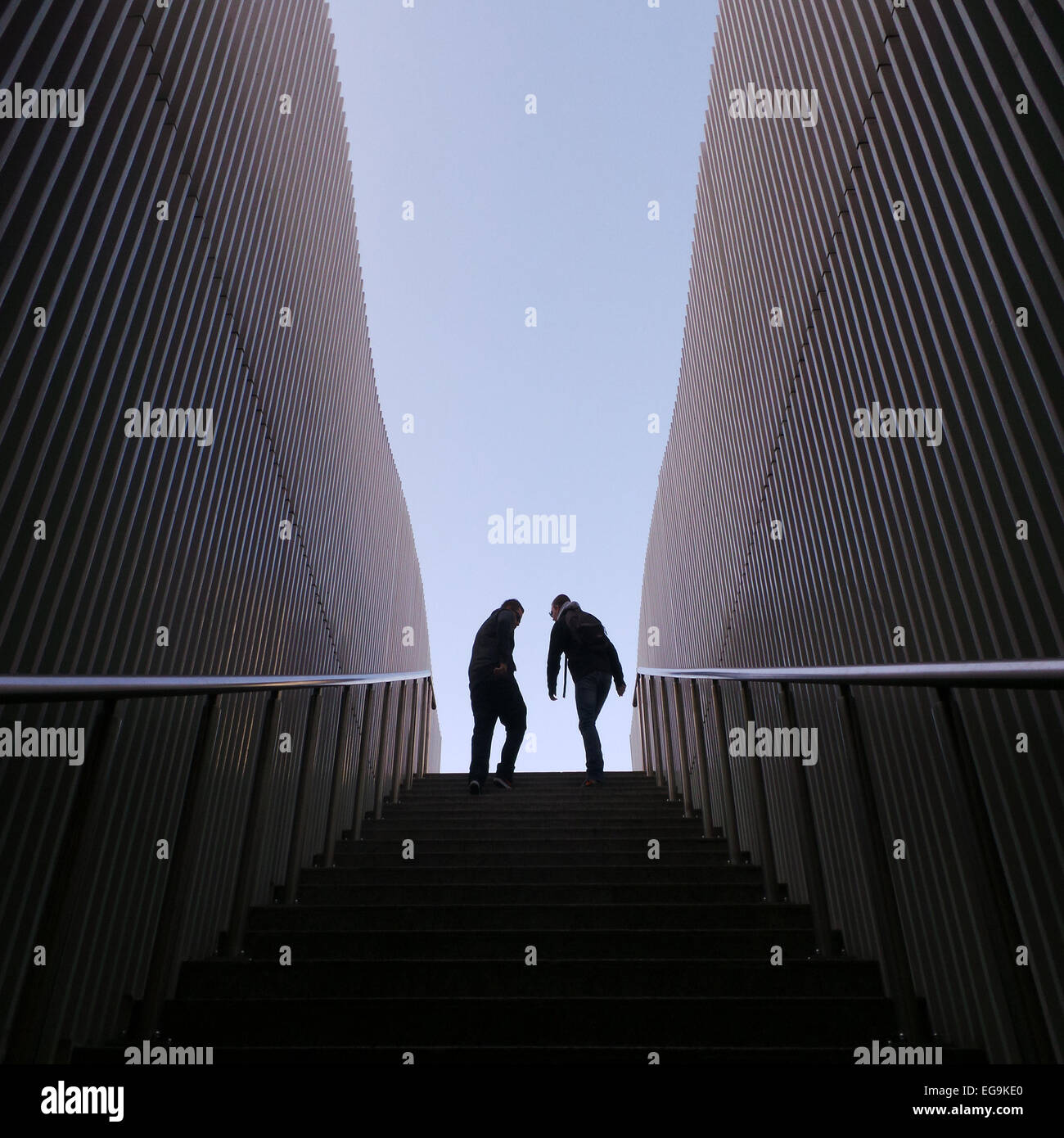 Imagen simétrica de dos personas de silueta en la parte superior de las escaleras, las paredes de los costados Foto de stock