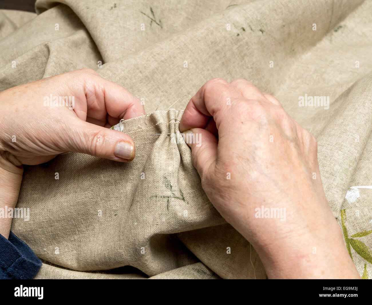 Primer plano de una mujer senior manos rociándolo frontera de lino con hilo y aguja Foto de stock