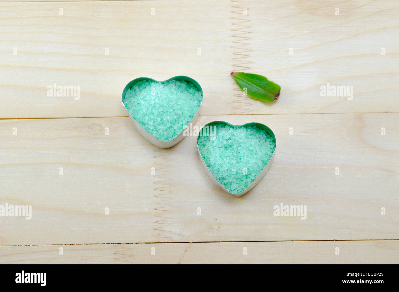 Verde mar de sal en una caja en forma de corazón en una mesa de madera con la hoja verde Foto de stock