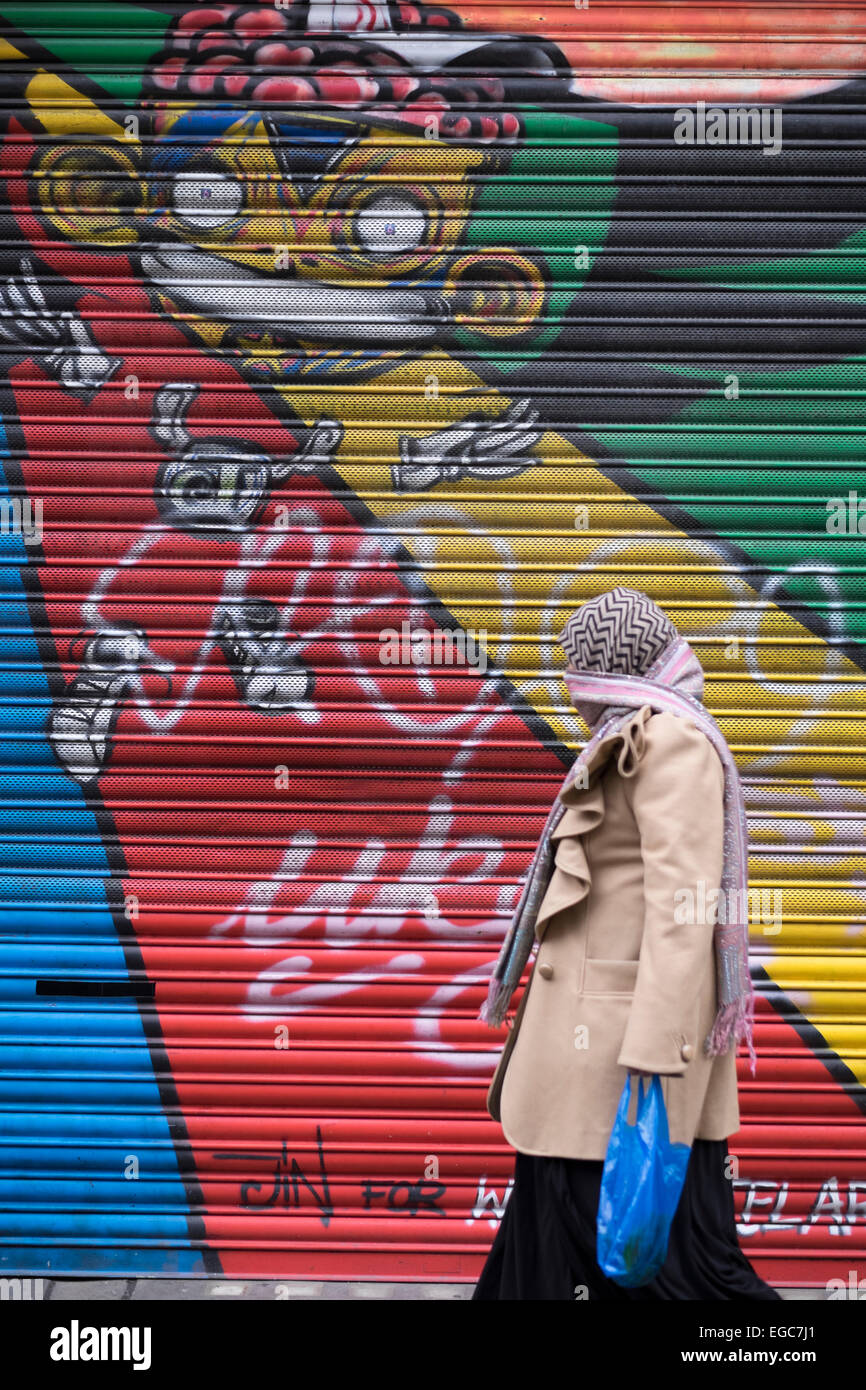 Señora musulmana ancianos paseando un cubierto de pintadas sobre moda Shop Front Street, London E1 Foto de stock