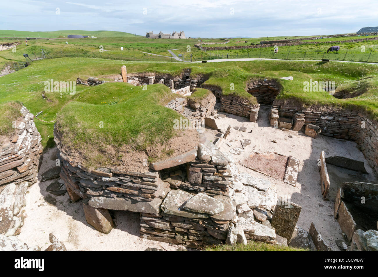 Casa 5 en Skara Brae aldea neolítica en el continente con las Islas Orcadas Skaill House en el fondo. Foto de stock