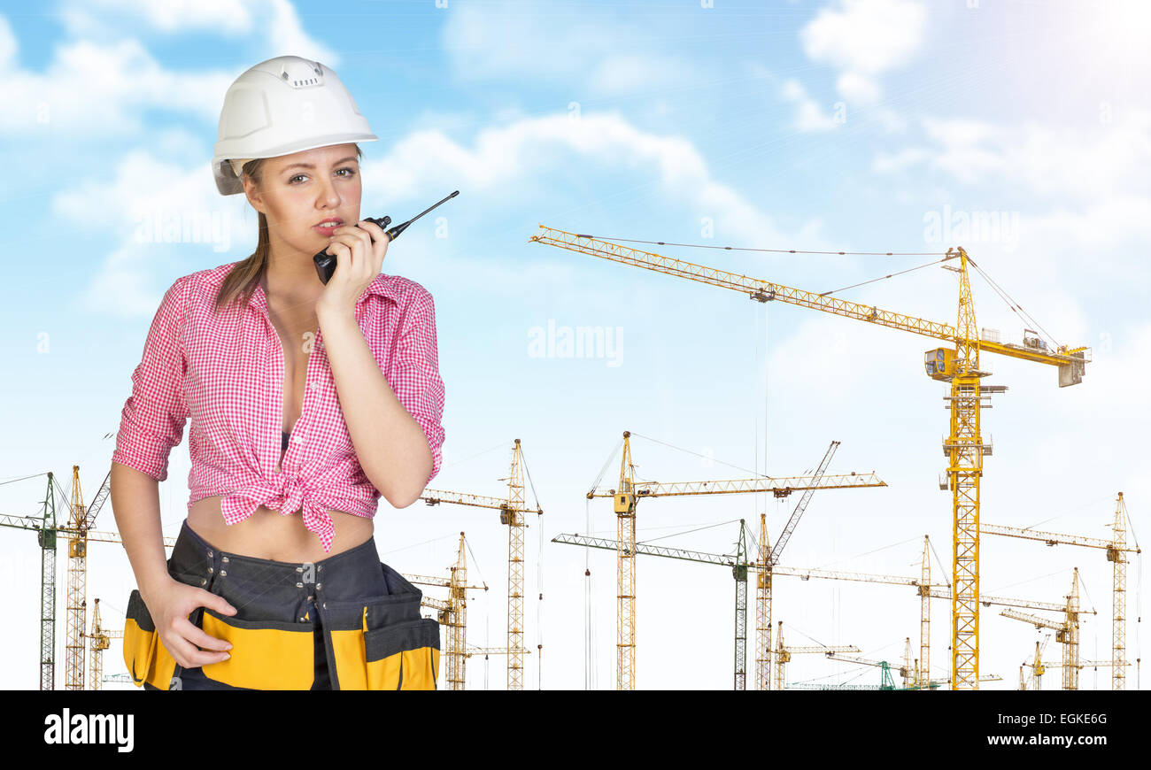 Mujer con sombrero duro y cinturón de herramientas hablando por un walkie-talkie Foto de stock