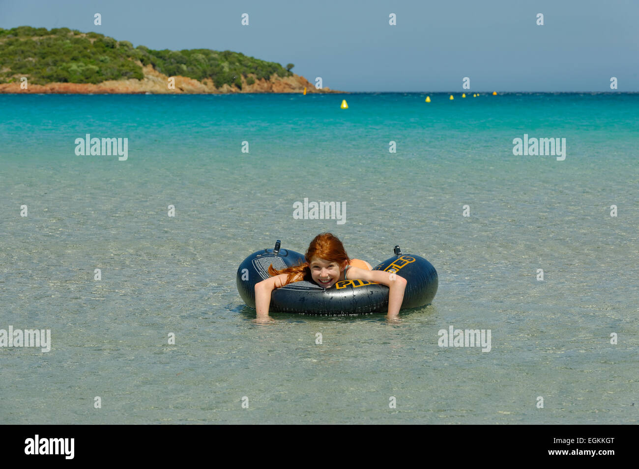 Una chica en grandes neumáticos flotantes en las aguas turquesas de la Bahía de Rondinara, costa sureste, Córcega, Francia Foto de stock