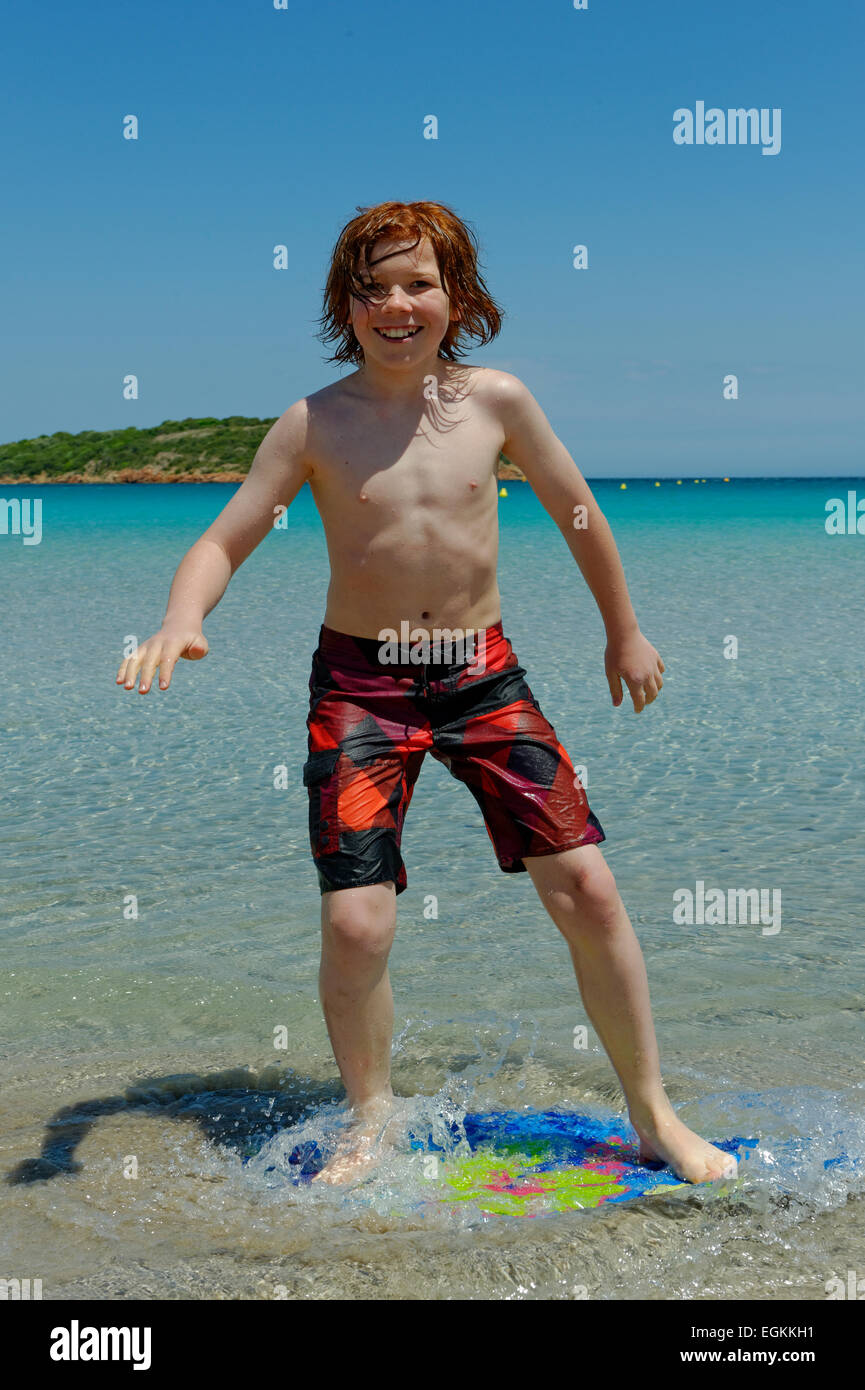 Boy navegando con su boggie board, junta de playa o skimboard en la playa, la bahía de Rondinara, costa sureste, Córcega, Francia Foto de stock