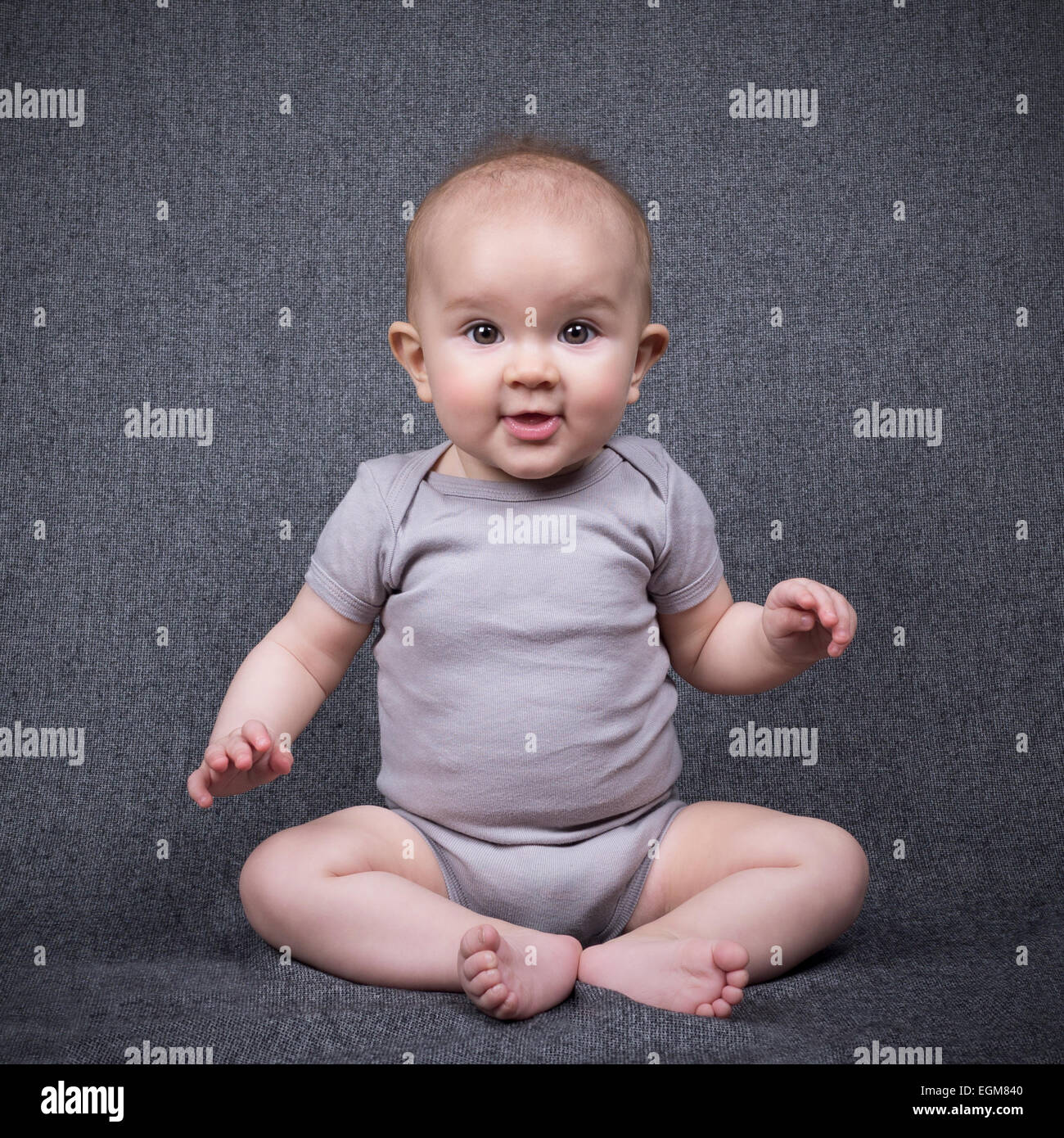 Adorable bebe sentado en el suelo sobre un fondo gris Foto de stock