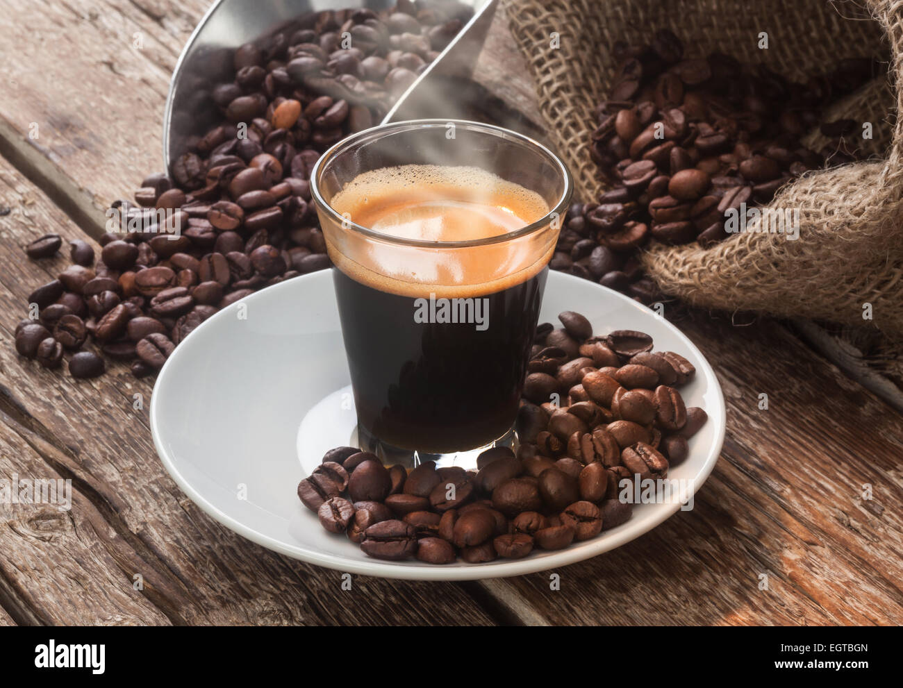 Café espresso en un vaso con granos de café sobre la mesa de madera. Foto de stock