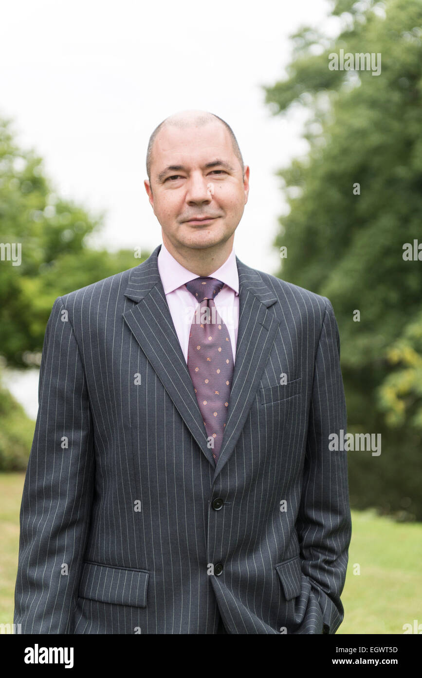 Un empresario profesional / gerente de hotel se encuentra en el jardín de una casa de campo inglesa hotel vistiendo un traje de negocios Foto de stock