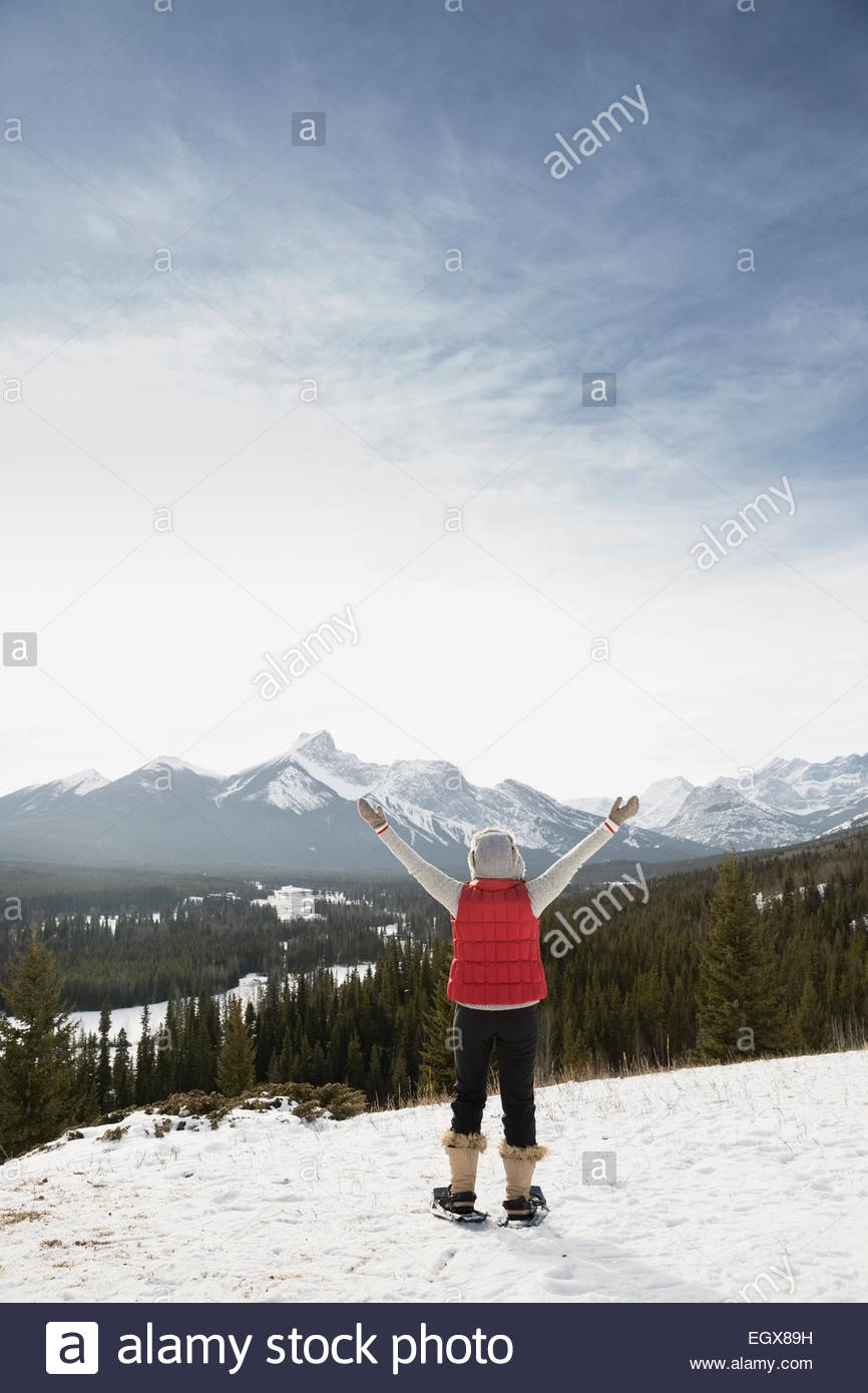 Exuberante mujer mirando con raquetas de nieve y montañas nevadas Foto de stock