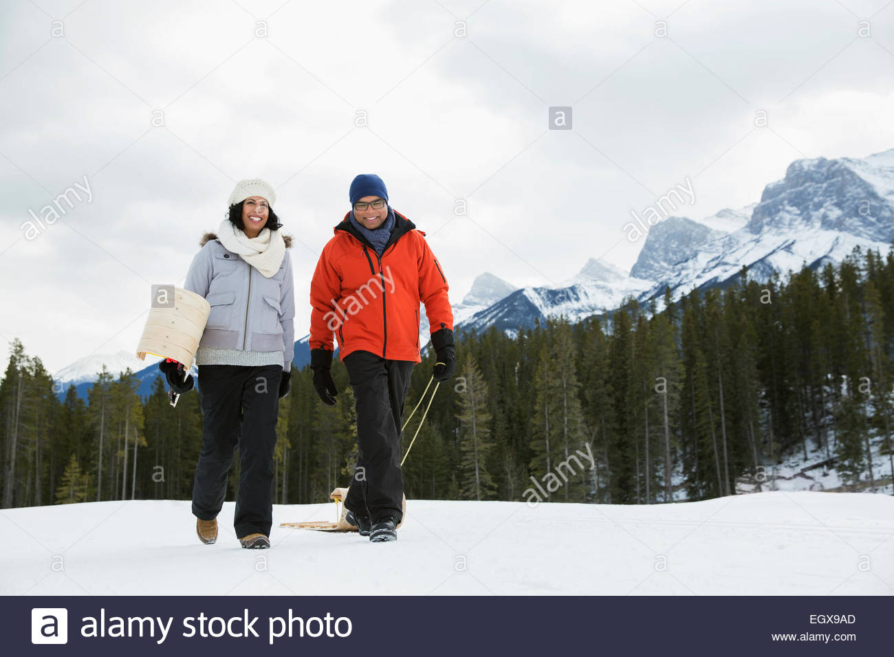 Pareja con trineos en campo nevado de montaña abajo Foto de stock