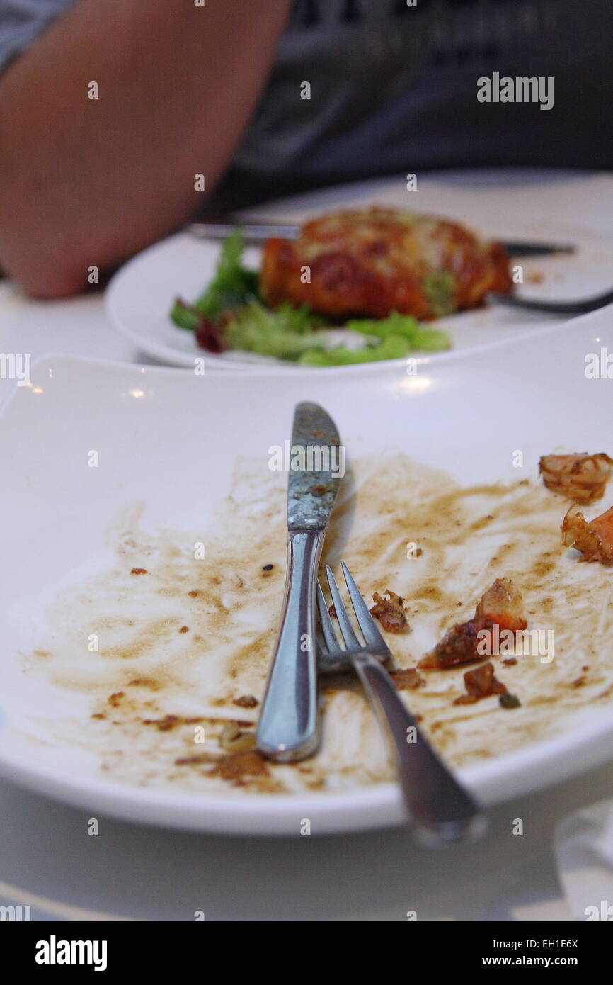 Cuchillo y tenedor sobre un plato vacío después de una comida Foto de stock