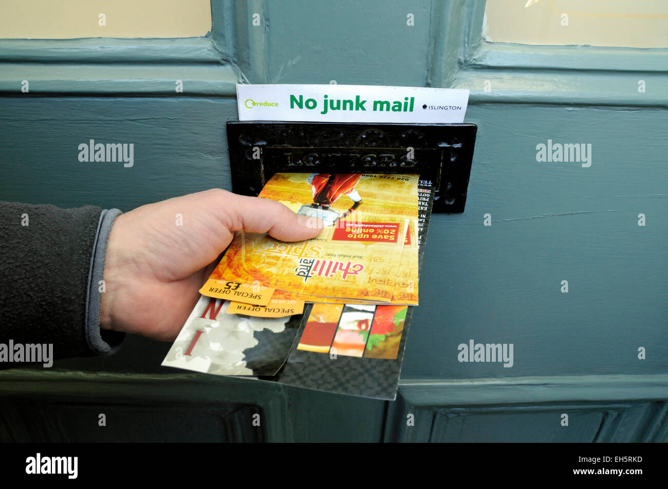 Mans mano empujando el correo no deseado a través del buzón de correo no deseado sin ningún signo de arriba, el distrito londinense de Islington, Inglaterra Foto de stock