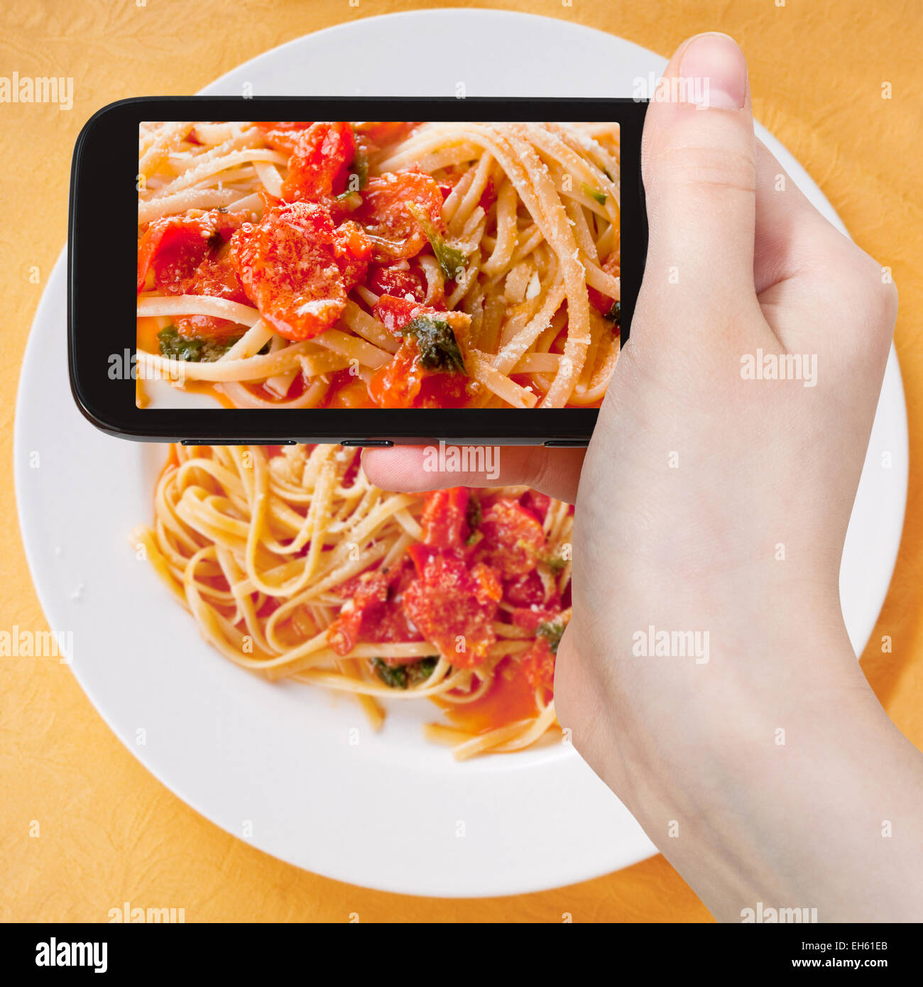 Fotografiar comida concepto - toma de fotografía turística de espaguetis con salsa de tomate picante sobre placa blanca en gadget móvil, Italia Foto de stock