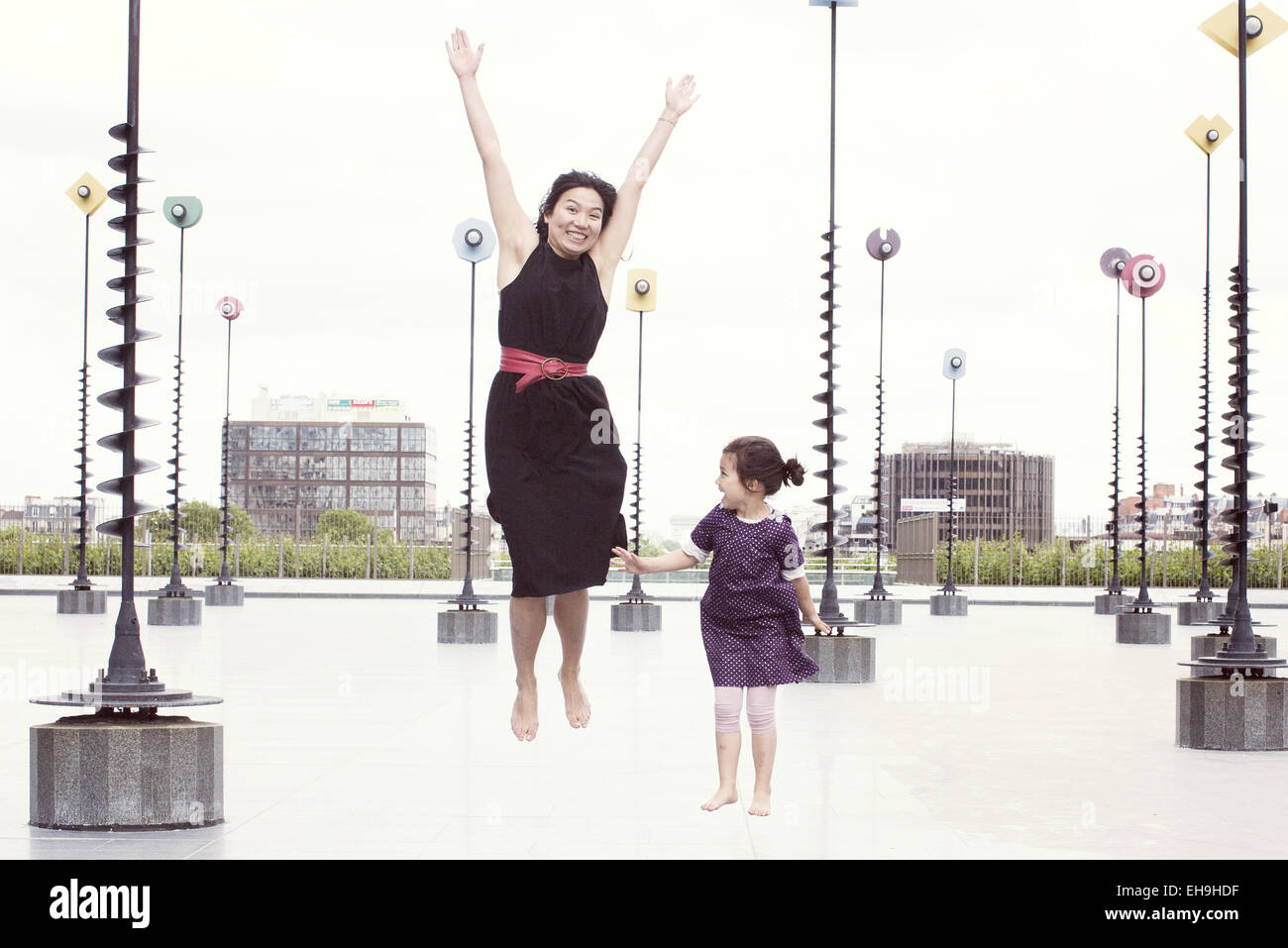 Madre e hija Saltando delante de whimiscal esculturas, La Défense, París, Francia Foto de stock