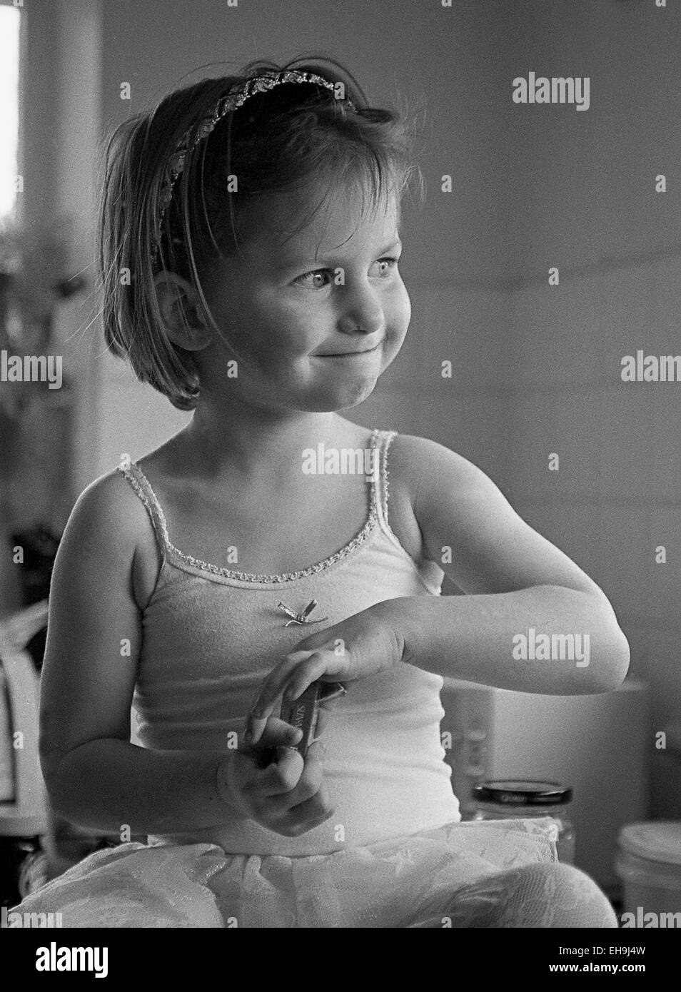 Imagen en blanco y negro de muy linda niña vestidos de tutu con encaje  guarnecido y arco pequeño en el centro. Asentada en la encimera de la  cocina, mirando hacia un lado